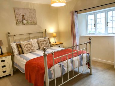 A bedroom with a white metal bed frame striped bedding and pillows with home sweet home text at Little Dragons Dunster near Minehead