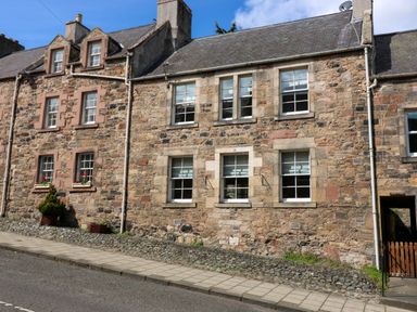 A stone residential building with multiple sash windows a sidewalk and a wooden gate at 49 Castlegate in Jedburgh