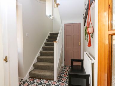 A hallway with patterned tile floor a staircase a wooden door a black bench and a hanging plant at 49 Castlegate in Jedburgh
