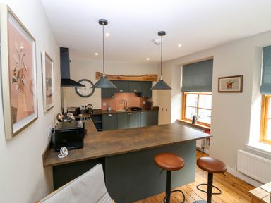 A kitchen with two hanging lamps two brown bar stools wooden floor and blue window blinds at 49 Castlegate in Jedburgh