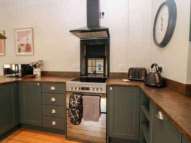 A kitchen with green cabinets a stove a microwave kettle and toaster at 49 Castlegate Jedburgh