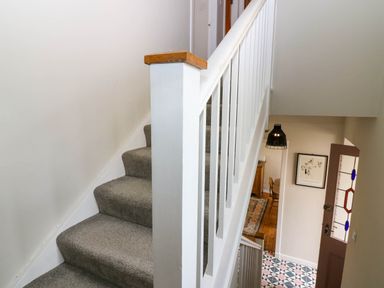 A staircase with grey carpet and white railing overlooking a hallway with patterned floor tiles and an open door at 49 Castlegate in Jedburgh