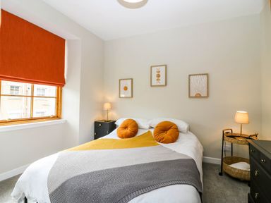 A bedroom with a double bed orange cushions bedside tables with lamps and framed pictures on the wall at 49 Castlegate in Jedburgh