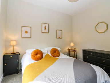 A bedroom with a bed with round pillows and a striped blanket bedside tables lamps and framed wall art at 49 Castlegate in Jedburgh