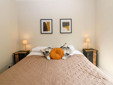 A bedroom with a bed two bedside tables with lamps and two framed artworks above the bed at 49 Castlegate in Jedburgh