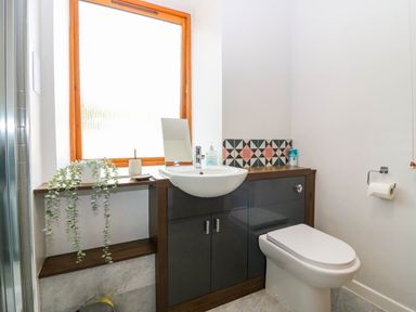 A bathroom with a toilet sink and wooden shelves under a frosted window at 49 Castlegate in Jedburgh