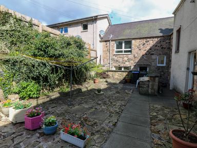 A stone patio with potted plants and a rotary clothesline in a backyard at 49 Castlegate in Jedburgh
