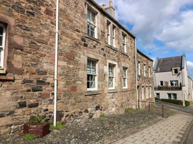 An exterior view of a stone building with windows and a sidewalk in front at 49 Castlegate in Jedburgh