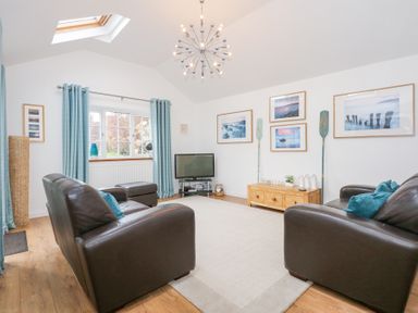 A living room with two brown leather sofas a TV on a stand blue curtains and framed pictures on the wall at Pippin Cottage in Beaumaris