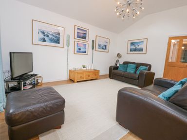 A living room with two brown leather sofas a brown leather ottoman a wooden coffee table a television on a black stand and framed pictures on the wall at Pippin Cottage in Beaumaris
