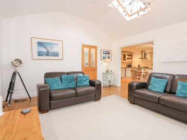 A living room with two brown leather sofas with blue cushions a tripod lamp and a wooden door leading to a kitchen at Pippin Cottage in Beaumaris