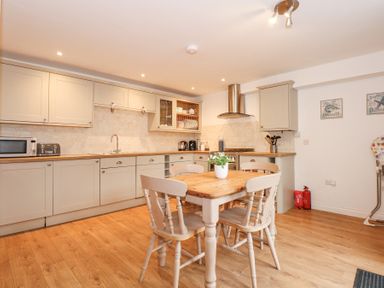 A kitchen with wooden floor cabinets a dining table with four chairs and a plant at Pippin Cottage in Beaumaris