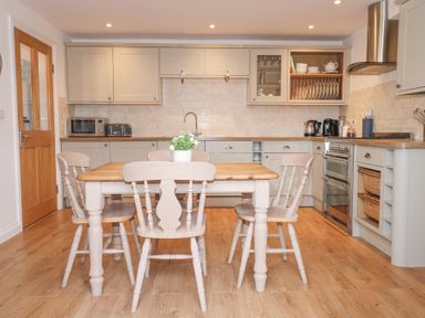 A kitchen with a wooden table and four chairs a plant on the table cabinets appliances and wooden floor at Pippin Cottage in Beaumaris