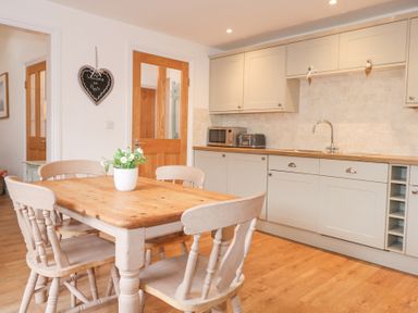 A kitchen with wooden dining table and chairs and white cabinets at Pippin Cottage in Beaumaris