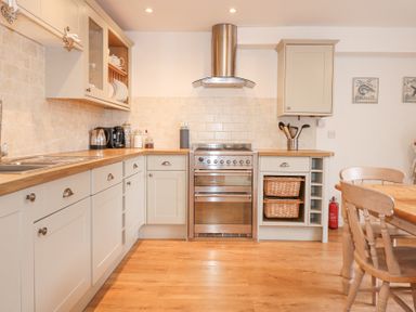 A kitchen with wooden countertops an oven and stovetop a sink coffee maker and dining table with chairs at Pippin Cottage in Beaumaris
