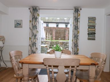 A dining room with a wooden table and chairs potted plant on table and open glass doors leading to an outdoor patio at Pippin Cottage in Beaumaris
