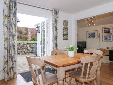 A dining area with a wooden table and four chairs a potted plant on the table and open doors leading to a patio at Pippin Cottage in Beaumaris