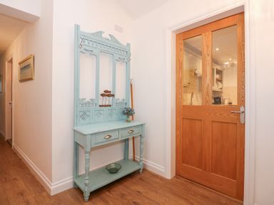 A hallway with a wooden floor a blue hall table with drawers a wooden door with glass panels showing part of a kitchen at Pippin Cottage in Beaumaris