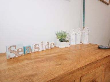 Wooden surface with decorative letters spelling Seaside small plants and three white birdhouse figures at Pippin Cottage in Beaumaris