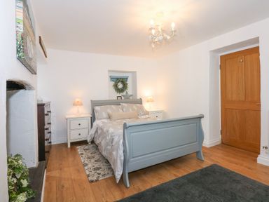 A bedroom with a blue bed frame bedside tables with lamps a wooden door and wooden floor at Pippin Cottage in Beaumaris