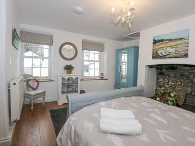 A bedroom with a bed folded towels a blue wardrobe a chair cabinet and two windows at Pippin Cottage in Beaumaris