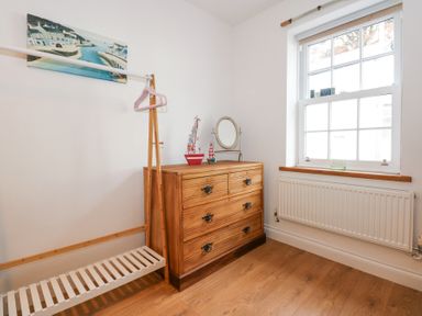 A room with a wooden dresser a standing mirror two model boats a wooden clothing rack with pink hangers and a window with a radiator below at Pippin Cottage in Beaumaris