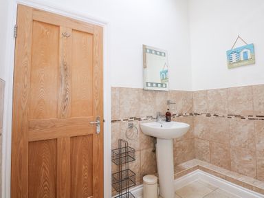 A bathroom with a wooden door a pedestal sink a mirror and beige tiled walls at Pippin Cottage in Beaumaris