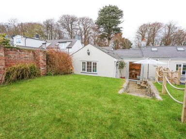 A grassy garden with a brick wall and patio area with a table and umbrella at Pippin Cottage in Beaumaris