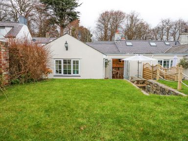 A garden with green grass and shrubs outside a white house with windows and a patio door at Pippin Cottage in Beaumaris