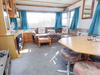 A living room with a corner sofa and blue curtains at Tanyfron Holiday Caravan in Bryngwran near Gwalchmai
