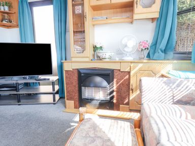 A living room with a television on a stand a fireplace and couches with blue curtains at Tanyfron Holiday Caravan in Bryngwran near Gwalchmai