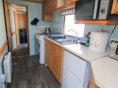 A narrow kitchen with wooden cabinets a stove sink microwave and refrigerator at Tanyfron Holiday Caravan in Bryngwran near Gwalchmai