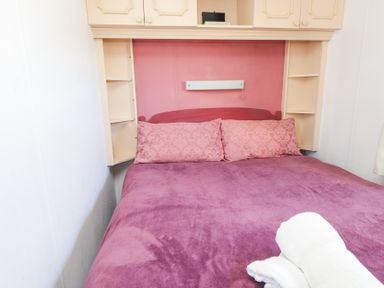 A bed with pink pillows and a purple blanket with shelves and cabinets above at Tanyfron Holiday Caravan Bryngwran near Gwalchmai
