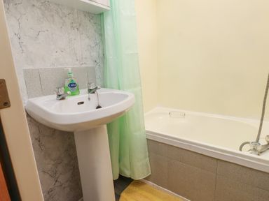 A bathroom with a white pedestal sink a green shower curtain a bathtub and a yellow rug at Tanyfron Holiday Caravan in Bryngwran near Gwalchmai