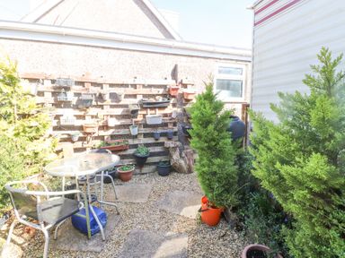 An outdoor garden area with a glass table and chairs surrounded by plants and pots at Tanyfron Holiday Caravan Bryngwran near Gwalchmai
