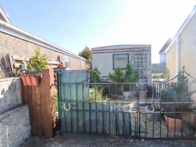 A view of a metal gate with potted plants and a caravan behind it at Tanyfron Holiday Caravan in Bryngwran near Gwalchmai