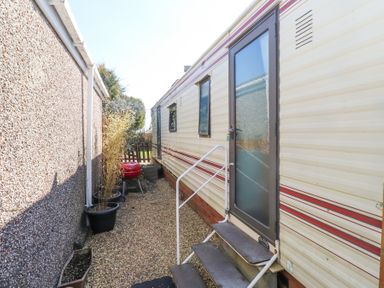 An exterior side view of a mobile home with stairs leading to a door and potted plants along a gravel pathway