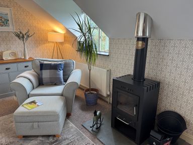 A snug with an armchair, ottoman, stove, and plant at The Hayloft in Lostwithiel