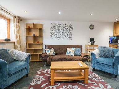 A living room with blue armchairs a brown sofa and a wooden coffee table at Oak Cottage in Aylesbeare