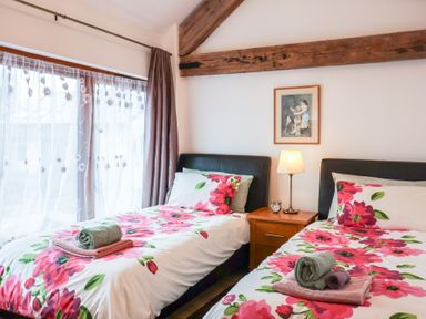 A bedroom with two single beds with floral bedding and a nightstand with a lamp and clock at Oak Cottage in Aylesbeare
