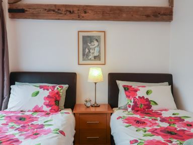 A bedroom with two single beds with floral bedding a bedside table with a lamp and alarm clock and a framed picture on the wall at Oak Cottage in Aylesbeare