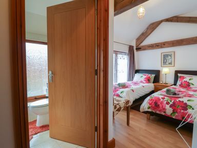 A bedroom with two single beds with floral bedding and a bathroom with a toilet and wooden door at Oak Cottage in Aylesbeare