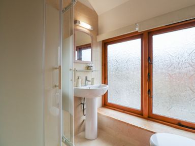 A bathroom with a pedestal sink mirror shower enclosure and frosted windows at Oak Cottage in Aylesbeare