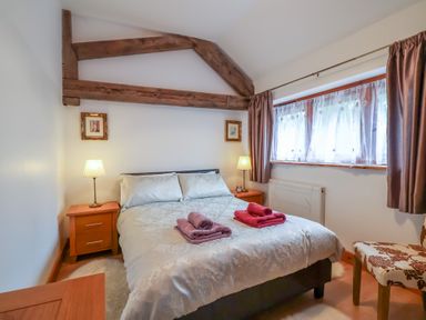 A bedroom with a double bed lamps and a window with curtains at Oak Cottage in Aylesbeare