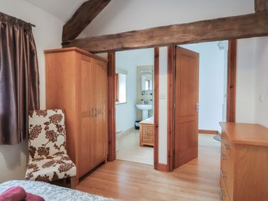 A bedroom with wooden wardrobe floral chair dresser and bathroom visible at Oak Cottage in Aylesbeare