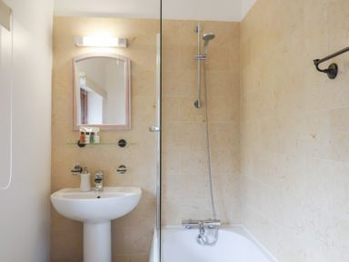 A bathroom with a sink and mirror and a bathtub with a shower at Oak Cottage in Aylesbeare