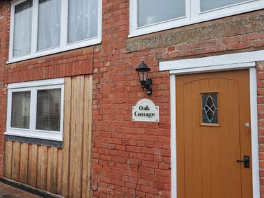 The front door and windows of a brick house with a sign reading Oak Cottage in Aylesbeare