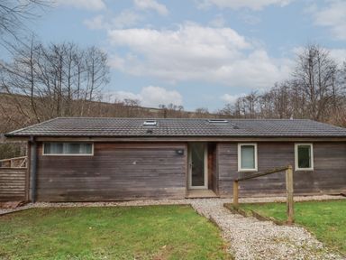 A single story wooden house with a tiled roof and three windows with a pathway and handrail at 2 Miller's Island Near Lanreath