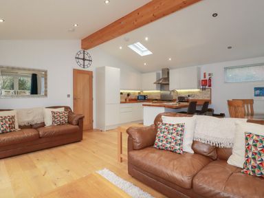 An open living area with brown leather sofas, a wooden coffee table, and a kitchen with white cabinets at 2 Miller's Island Near Lanreath