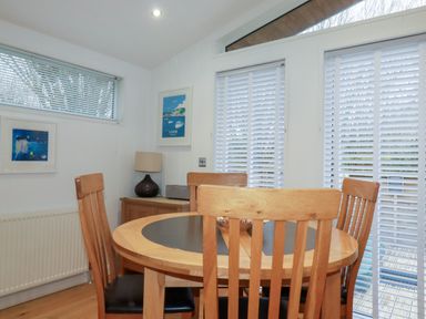 A dining area with a round wooden table and four chairs near windows with blinds at 2 Miller's Island Near Lanreath